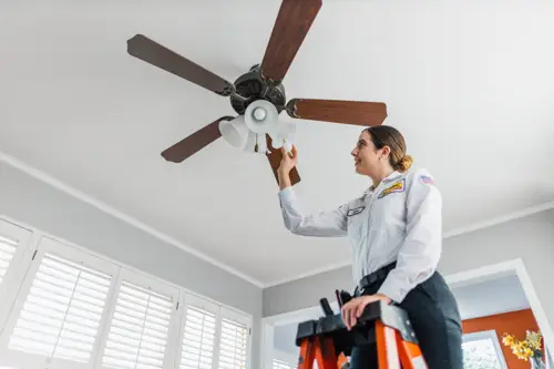 Mister Sparky Electrician Tech, Jane, finishing up a ceiling fan installation by screwing in the last light bulb